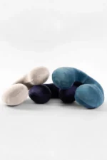 Three plush, curved Travel Neck pillows resembling bent arms are intertwined. They are light beige, navy blue, and teal, set against a minimalist white background.