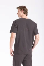 Young man in a gray Medical Scrub, standing with his back to the camera, looking over his shoulder against a plain white background.