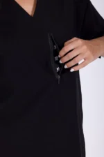 A close-up of a black scrubs top with a woman's hand reaching into a zippered pocket lined with a playful flower pattern.