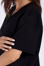 Close-up of a woman in a black shirt, gently resting her hand on her sleeve, showcasing a casual and stylish look.