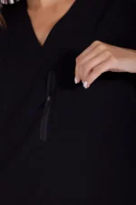A close-up of a woman wearing a black scrub top with a zippered pocket, gently touching the pocket with her hand.