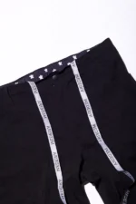 Close-up image of the waistband area of a pair of black scrub pants, featuring a button closure and an inner drawstring with the repeated text "WEDEIYA" printed in bold, black uppercase letters on a white background. The inner waistband lining showcases a pattern of white medical cross symbols on a navy blue fabric. The pants also include belt loops and visible stitching, highlighting a functional, professional design ideal for healthcare uniforms.