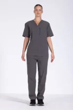 Full-body image of a woman wearing dark grey medical scrubs, featuring a V-neck short-sleeve scrub top with a vertical zippered chest pocket on the left side and matching straight-leg scrub pants with a side cargo pocket. She is standing against a plain white background and wearing black athletic shoes. The outfit is professional healthcare attire, suitable for nurses, doctors, and medical staff.
