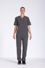 Full-body image of a woman wearing gray medical scrubs, featuring a V-neck short-sleeve scrub top with a vertical zippered chest pocket on the left side and matching straight-leg scrub pants with a side cargo pocket. She is standing against a plain white background and wearing black athletic shoes. The outfit is professional healthcare attire, suitable for nurses, doctors, and medical staff.