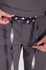 Hands adjusting the waistband of gray pants, revealing a black inner fabric with white floral patterns and a drawstring labeled "MEDEIRA," conveying functionality and style.